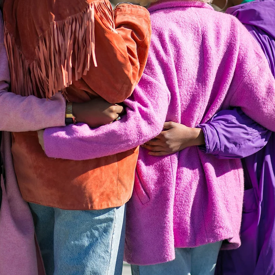 Women in colour coats hugging each other
